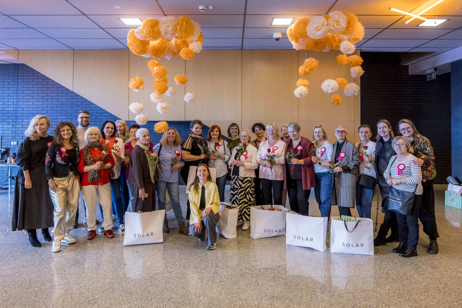 Grupa Mam i organizatorek stoi razem do zdjęcia, wiele z nich trzyma kwiaty i torby Solar. Wspólna fotografia podsumowuje dzień spędzony podczas „Oddechu dla Mam”.